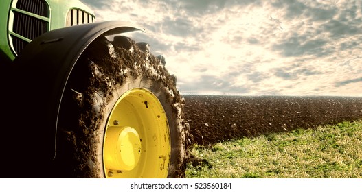 Agriculture. Tractor plowing field. Wheels covered in mud, field in the backround. Cultivated field. Agronomy, farming, husbandry concept.