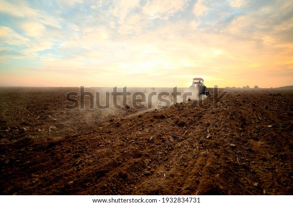 Agriculture use tractor plowing land field in the\
backround. Cultivated field. Agronomy, farming, husbandry .Tractor\
working on farm at sunset,modern agricultural transport,farmer\
working in the\
field