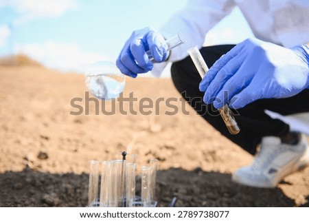 Agronomist crouching, studying soil samples in test tubes and flasks, conducting agricultural research in a field