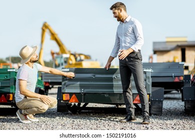 Agronomist With Salesman Choosing A New Farm Truck Trailer, Standing On The Open Ground Of The Agricultural Shop