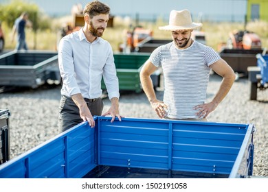 Agronomist With Salesman Choosing A New Farm Truck Trailer, Standing On The Open Ground Of The Agricultural Shop