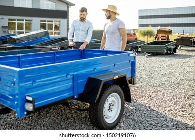 Agronomist With Salesman Choosing A New Farm Truck Trailer, Standing On The Open Ground Of The Agricultural Shop