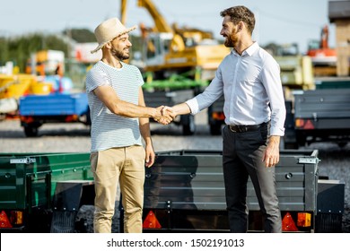 Agronomist Shaking Hand With Salesman, Buying A New Farm Truck Trailer On The Open Ground Of The Agricultural Shop