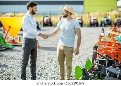 Agronomist Shaking Hand With Salesman, Having A Deal About Purchase A New Agricultural Machinery On The Outdoor Ground Of The Shop