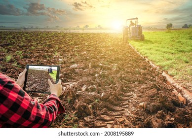 Agronomist using tablet in field while tractor plows soil for planting. Agriculture technology farmer using tablet computer analysis data.modern technology application in agricultural growing activity