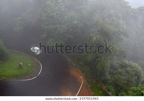 Agumbe Ghats or Hill Station, Maharashtra, India\
- August 7 2022: An aerial shot of a car traveling on the foggy\
forest road. Low visibility due to thick fog. The Car might be\
blurred due to motion.