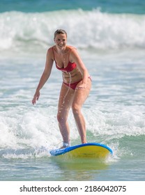 Ahangama, Sri Lanka - 04 17 2022: A Wet Woman In A Red Bikini Is Surfing On The Tropical Beach, Leaning Forward And Riding With A Small Wave.