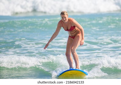 Ahangama, Sri Lanka - 04 17 2022: A Wet Woman In A Red Bikini Is Surfing On The Tropical Beach, Leaning Forward And Riding With A Small Wave.