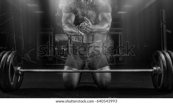 Ahlete kneels in the gym
before the bar and claps his hands after which the dust from the
chalk flies