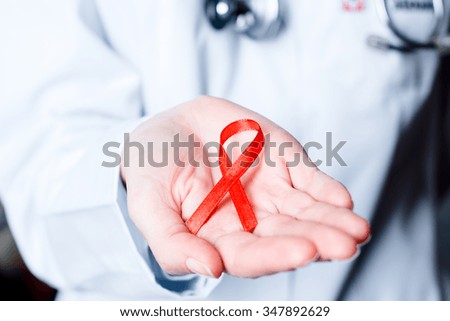AID, HIV red ribbon. Symbol of awareness, charity, support in disease, illness, ill. Medical health care, help and hope. Sign of healthcare medicine campaign holding in female doctor hand. 
