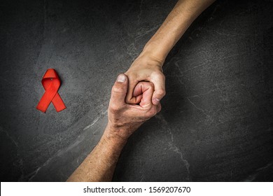 AID red ribbon in hand on gray background, symbol of the fight against HIV, AIDS and cancer. concept of helping those in need