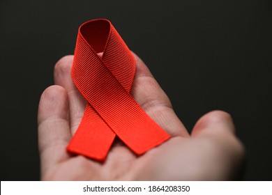 AID red ribbon in hand on gray dot background, symbol of the fight against HIV, AIDS and cancer. concept of helping those in need, close-up photo - Powered by Shutterstock