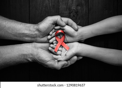 AID red ribbon in hands on a black wooden background, World Cancer Day, symbol of the fight against HIV, AIDS and cancer. concept of helping those in need. black and white.