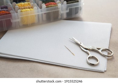 Aida white canvas, needle, needlework scissors and a box with multicolored embroidery threads, needlework and cross stitch concept