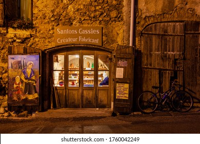 Aiguines, France - July 8, 2011: Night View Of Figurine Store Santons Gassies. Light Inside, Rustic Retro Style Architecture.Bicycle Left Next To Door.