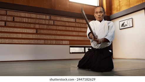 Aikido with sensei on floor, wooden sword and training for fitness, fight or action in traditional gym in Japan. Exercise, practice and mature man at dojo with black belt in Japanese martial arts.