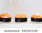 air of chopsticks positioned to select a piece from a trio of spicy baked sushi nigiri or salmon gunkans on white background