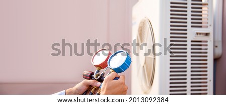Air condition mechanic using manifold gauge for filling home air conditioner and checking maintenance and repair outdoor air compressor unit.