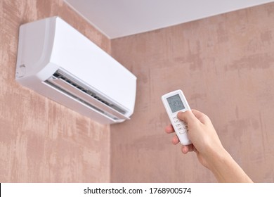 Air Conditioner At Domestic Room. Heat Temperature Indoors. Person Holds Remote Control For Aircon. Heat Or Cold At Home.