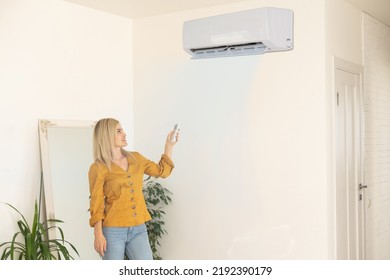 Air conditioner inside the room with woman operating remote controller. Air conditioner with remote controller - Shutterstock ID 2192390179