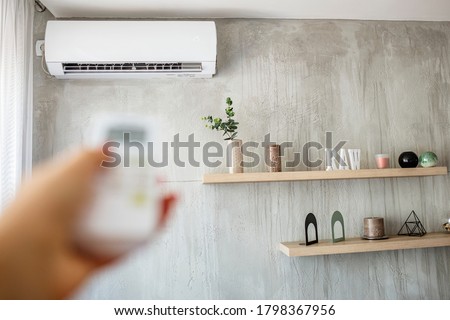 Air conditioner inside the room with woman operating remote controller. / Air conditioner with remote controller. Close up view of hand operating air conditioner remote control. 