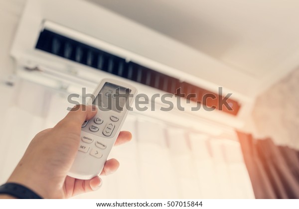 Air conditioner\
inside the room with woman operating remote controller. / Air\
conditioner with remote\
controller
