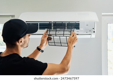 Air conditioner maintenance. Male technician repairs home climate system in living room. Man is cleaning filters of conditioner