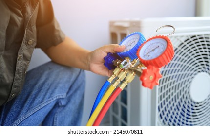 An Air Conditioner Technician's Hand Holding A Manifold Gauge To Check The Pressure Inside The System To Normalize The Refrigerant Charge During High Temperatures And Hot Weather. Maintenance Concept.