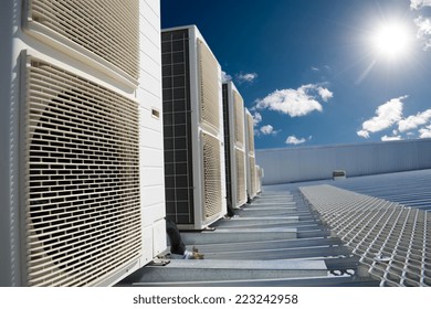 Air conditioner units (HVAC) on a roof of industrial building with blue sky and clouds in the background.