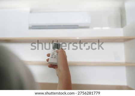 Air Conditioning Control. Hand using remote to adjust temperature settings.