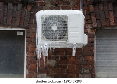 Air conditioning covered with ice and icicles on brick wall/danger for passers, сold winter, poor thermal insulation, ice stalactite, formation of icicles, frost and winter weather concept.