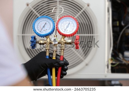 Air conditioning electrical technician using manifold gauge measuring tool checking refrigerant pump filling home air conditioner and maintenance heat fix repair and clean outdoor compressor unit.