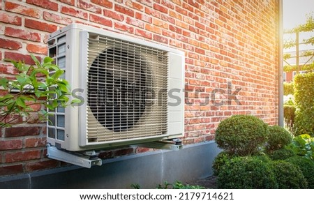 Air conditioning heat pump outdoor unit against brick wall.