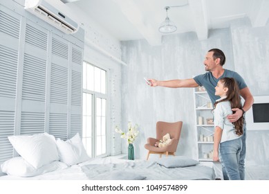 Air conditioning. Positive delighted joyful man standing together with his daughter and looking at the air conditioner while holding a remote control