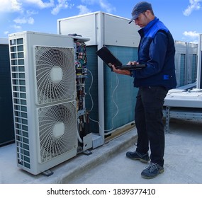 air conditioning technician making a diagnosis of an industrial air conditioning unit with a laptop next to other VRV condenser units on a rooftop in a sunny day - Powered by Shutterstock