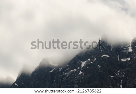 Air element. The cloud is stuck in the snowy rocky peak of the high mountain. Wind, clouds, bad weather, before storm, dangerous climbing theme. Concept of climate