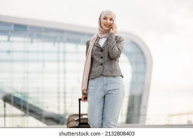 Air flight journey and business concept. Pretty traveler tourist arabian woman in hijab carrying suitcase and talking phone, walking near modern airport terminal