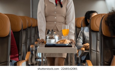 Air hostess or cabin crew working in airplane. Flight attendant pushing the cart on aisle for serving food and drink to passengers in airplane cabin. Airline transportation and tourism concept.