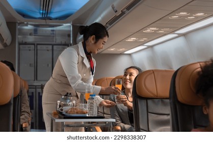 Air hostess or cabin crew working in airplane. Female flight attendant serving orange juice to businesswoman passenger on board. Airline transportation and tourism concept.