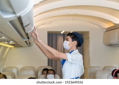 Air hostess or stewardess wearing protective face mask checking luggage cabin on the airplane