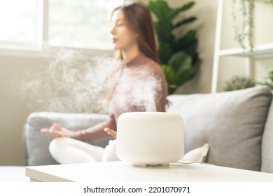 Air humidifier, calm blurred woman, girl sitting on couch lotus pose put hands practice meditation do yoga exercise at home. Aromatherapy steam scent from essential oil diffuser in living room at home - Powered by Shutterstock