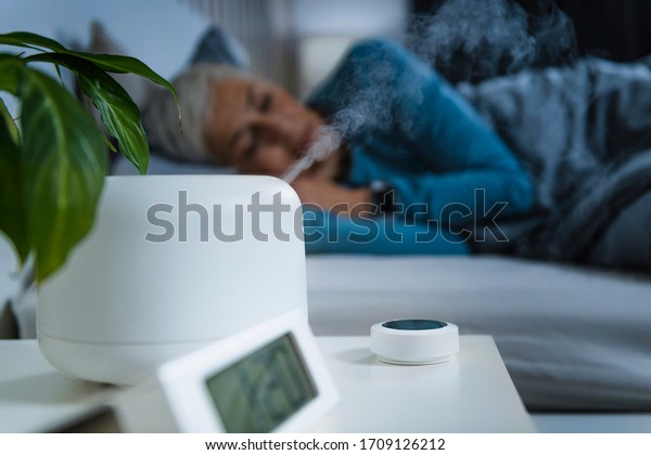 Air Humidifier\
increasing the humidity in a bedroom for better sleep. Beautiful\
mature woman sleeping in\
bed.