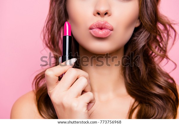 Air kiss for\
you. Close up cropped shot of femenine gorgeous charming adorable\
lady with amazing wavy hair do, tube of hard pink pomade in arm.\
Pampering, lips correction\
concept