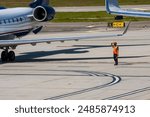 An air marshaller wearing an orange safety vest directing a commercial jet on a tarmac