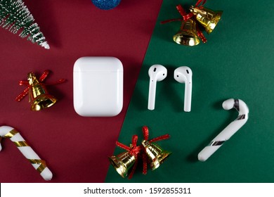 Air Pods. With Wireless Charging Case. New Airpods 2020 On Red And Green Background. Air Pods On Christmas Background. Christmas Headphones