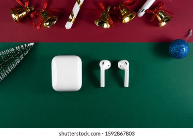 Air Pods. With Wireless Charging Case. New Airpods 2020 On Red And Green Background. Air Pods On Christmas Background. Christmas Headphones