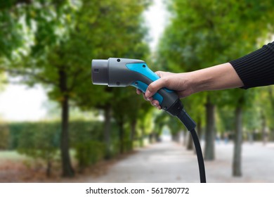 Air Pollution And Reduce Greenhouse Gas Emissions Concept. Hand Holding And Charging Electric Car With Green Natural Garden View Background.