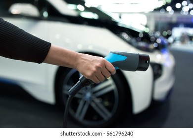 Air Pollution And Reduce Greenhouse Gas Emissions Concept. Hand Holding And Charging Electric Car With Blur Electric Car View Background.