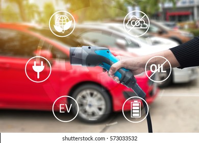 Air Pollution And Reduce Greenhouse Gas Emissions Concept. Hand Holding Electric Charging Vehicle Car And Icons With Blur Cars Background.