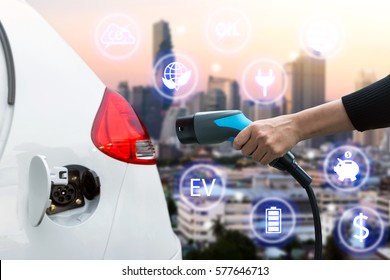 Air Pollution And Reduce Greenhouse Gas Emissions Concept. Hand Holding And Charging Electric Car With Blur City View Background.